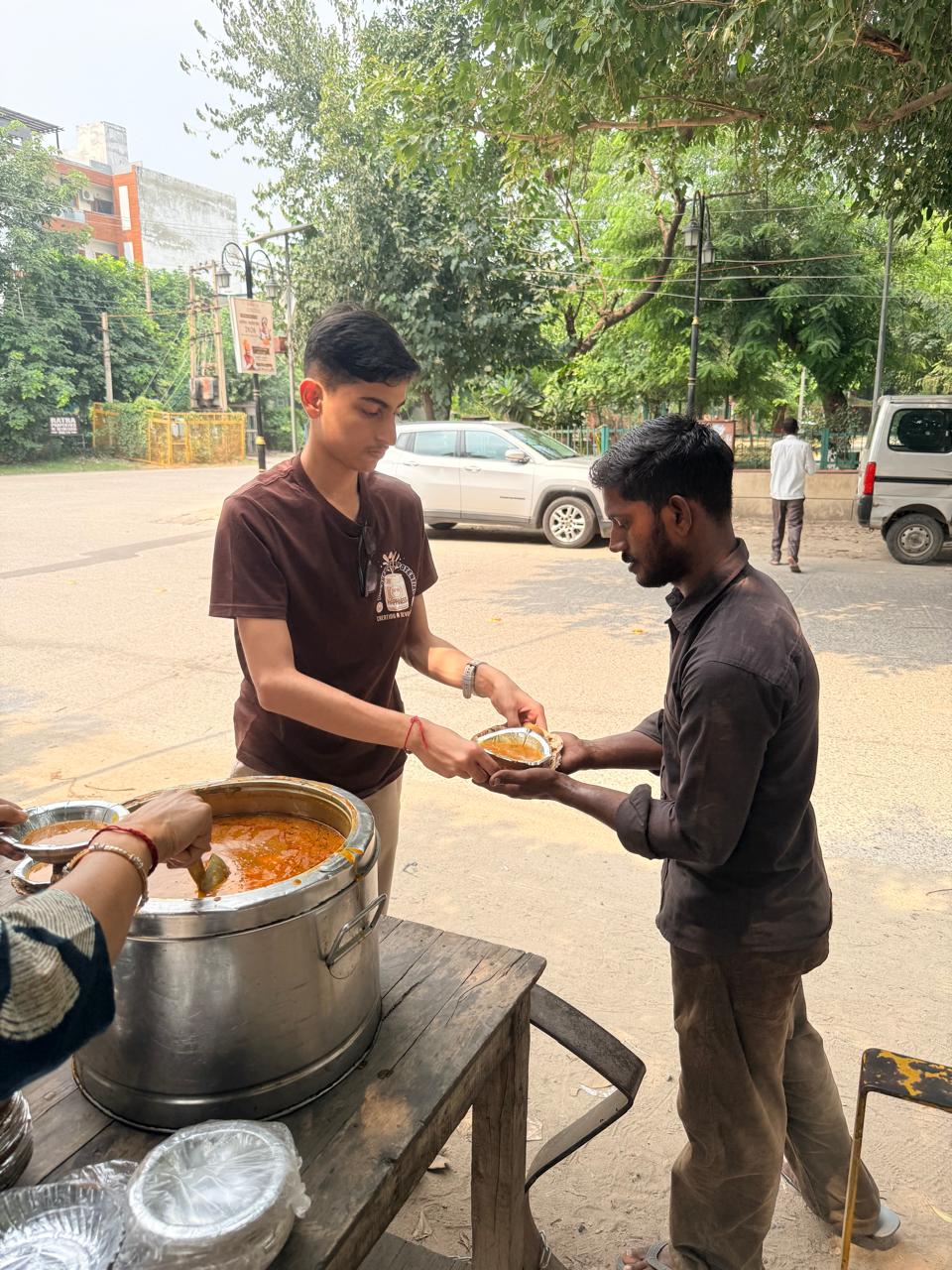 Jinanssh Jain handing a prepared meal to a community member during Nourish All on 20 September 2026 in Sector 14, Faridabad.