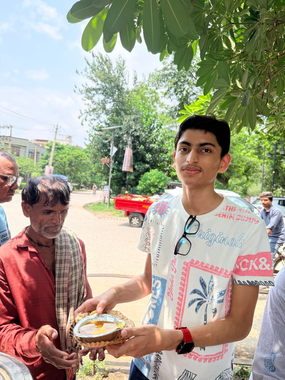 Jinanssh Jain holding a meal plate beside a community member during Nourish All.