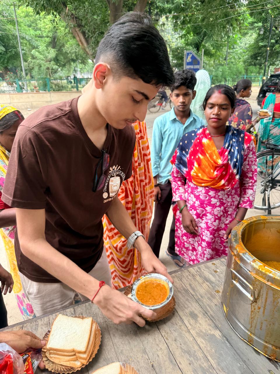 Jinanssh Jain assembling a meal plate while community members stand nearby during Nourish All.